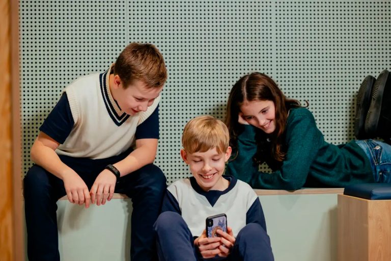 Tre børn og sider sammen og kigger på mobiltelefon